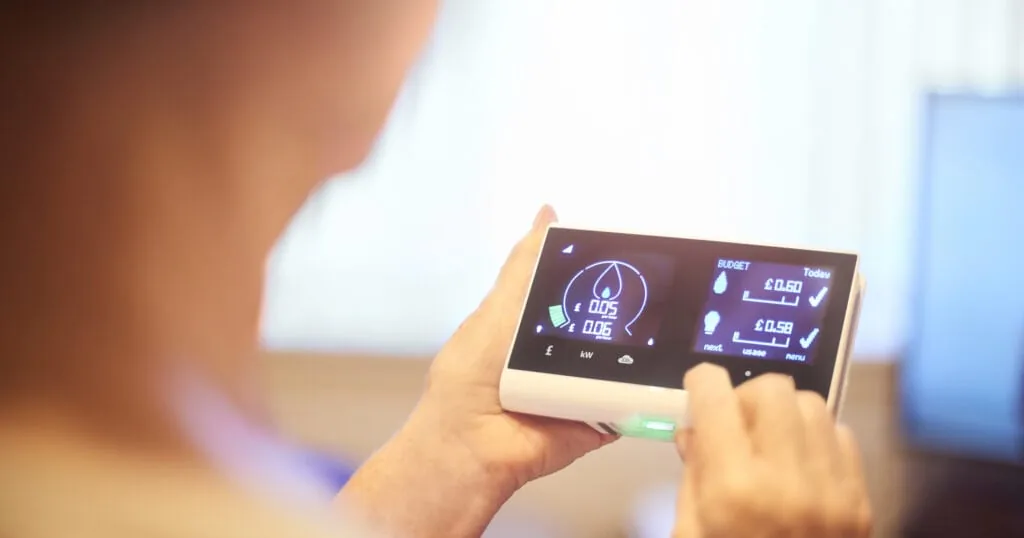 Person holding a smart meter in-home display showing live energy usage and daily budget